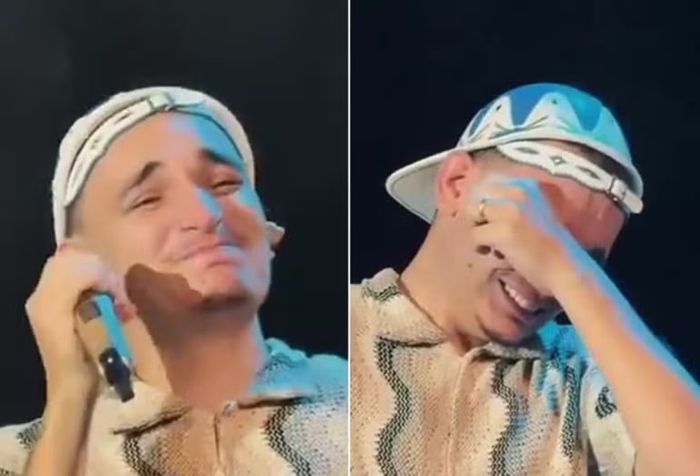 O cantor João Gomes com a mão no rosto ou emocionado no palco, em um momento de homenagem à sua professora presente na plateia em Petrolina.