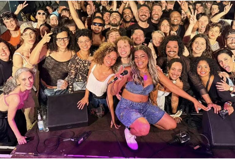 A cantora Tati Quebra Barraco em um palco, durante um show na Europa, com a plateia animada.